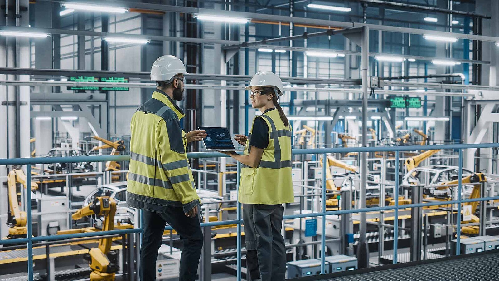2 Personen stehen mit Helmen und Arbeitskleidung in den Produktionshallen